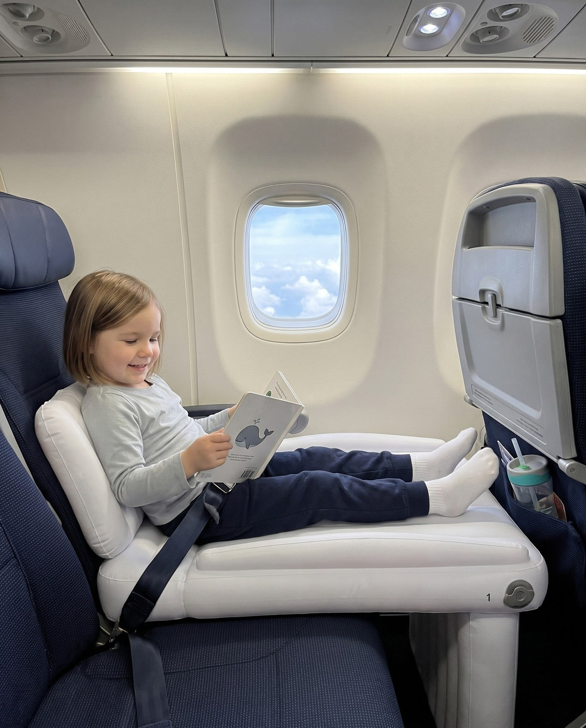 Child sitting on a Travel Nest Kids Bed in an airplane seat, playing during the flight