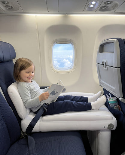 Child sitting on a Travel Nest Kids Bed in an airplane seat, playing during the flight